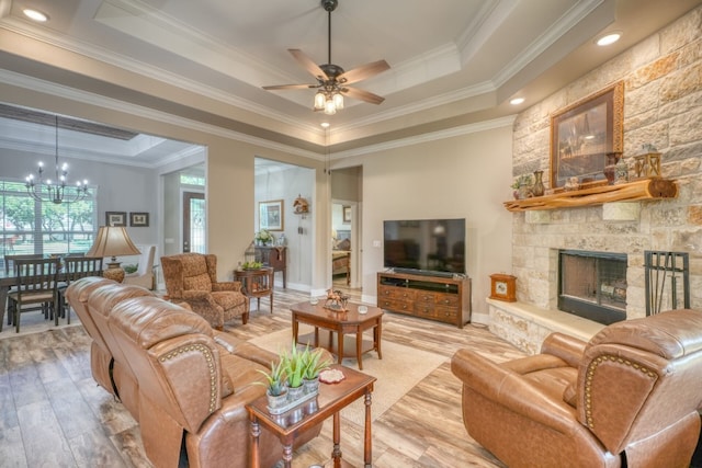 living room with light wood-style flooring, ornamental molding, a raised ceiling, and a stone fireplace