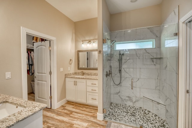 full bathroom with a marble finish shower, a spacious closet, wood finished floors, and vanity