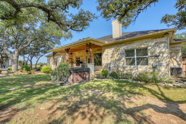 rear view of house featuring stone siding, a hot tub, a chimney, and a lawn