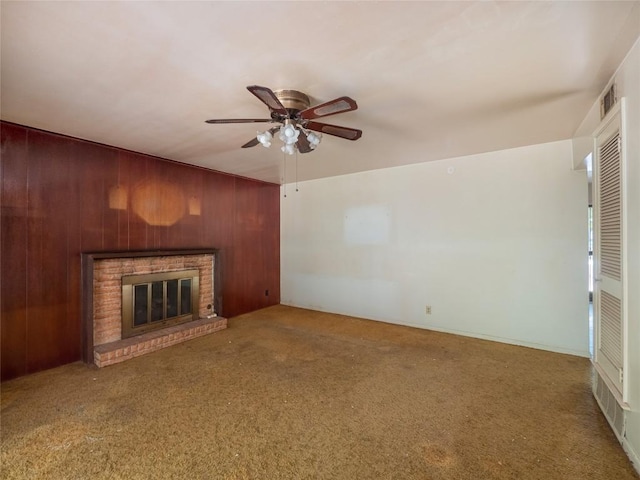 unfurnished living room with a brick fireplace, carpet, wood walls, and ceiling fan