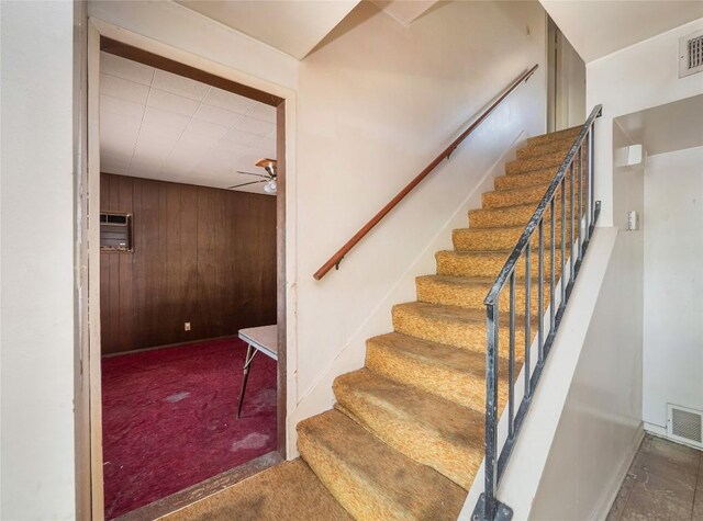 staircase featuring wood walls, a wall unit AC, ceiling fan, and carpet floors