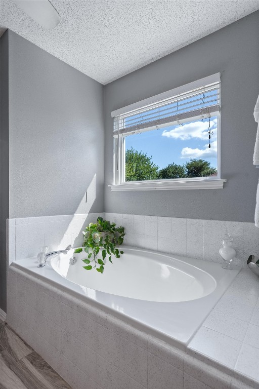 bathroom with tiled tub and a textured ceiling