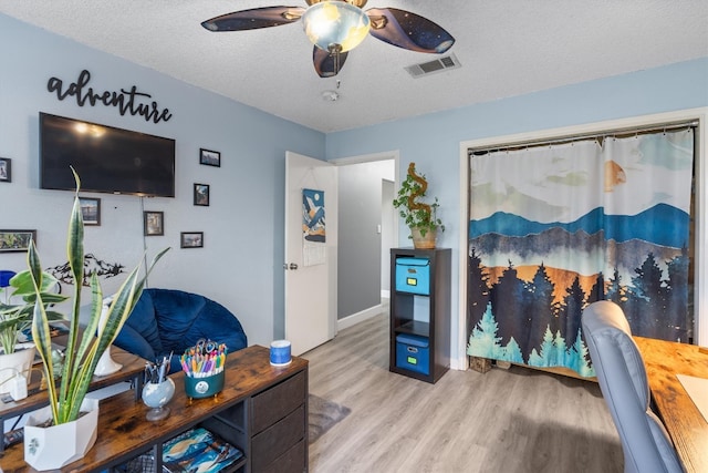 living room with ceiling fan, a textured ceiling, and wood-type flooring