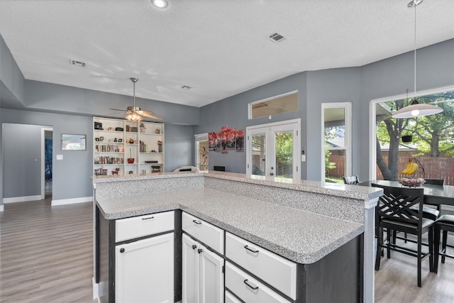 kitchen featuring white cabinetry, light wood-type flooring, a textured ceiling, ceiling fan, and hanging light fixtures