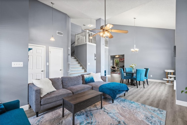 living room featuring a textured ceiling, high vaulted ceiling, ceiling fan with notable chandelier, and light wood-type flooring