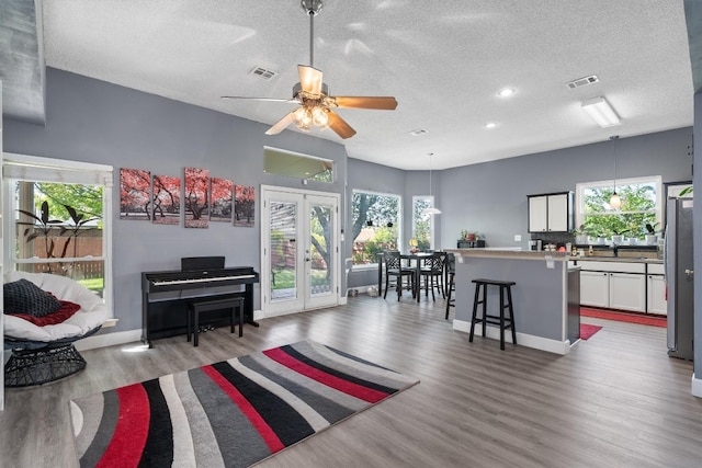 living room featuring ceiling fan, a textured ceiling, light hardwood / wood-style floors, and a healthy amount of sunlight