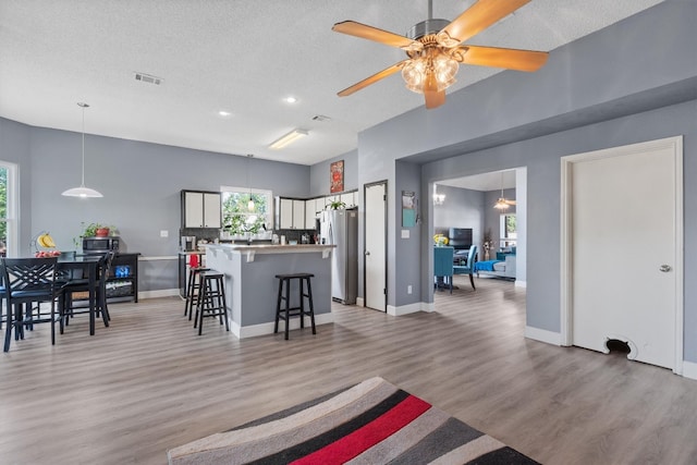 kitchen with ceiling fan, light wood-type flooring, a kitchen breakfast bar, white cabinets, and stainless steel fridge