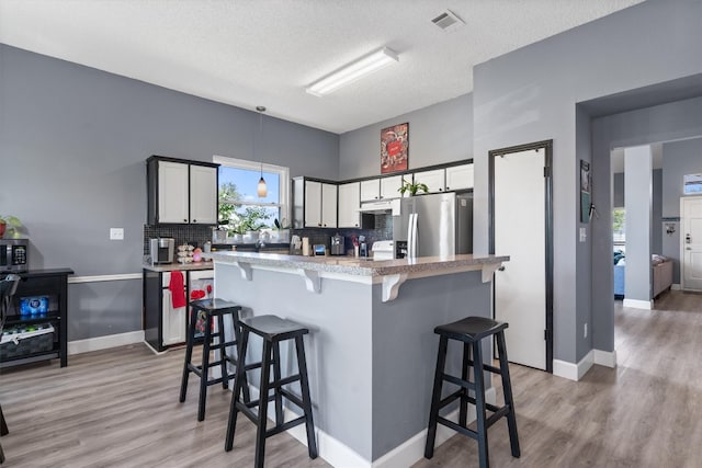 kitchen featuring a kitchen breakfast bar, light wood-type flooring, appliances with stainless steel finishes, tasteful backsplash, and white cabinetry