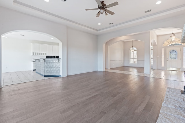 unfurnished living room featuring light wood-type flooring, ceiling fan with notable chandelier, and a tray ceiling