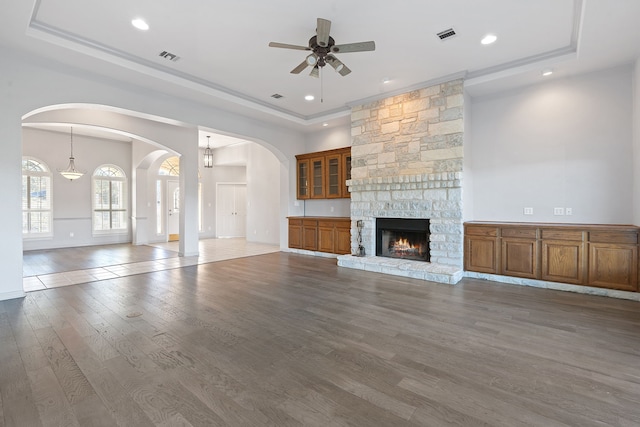 unfurnished living room with hardwood / wood-style flooring, ceiling fan, a fireplace, and a tray ceiling