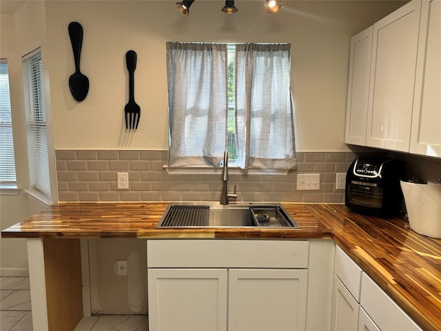 kitchen featuring a wealth of natural light, decorative backsplash, white cabinetry, a sink, and wood counters