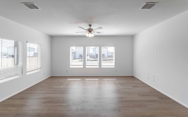 empty room featuring ceiling fan, hardwood / wood-style flooring, a textured ceiling, and a wealth of natural light