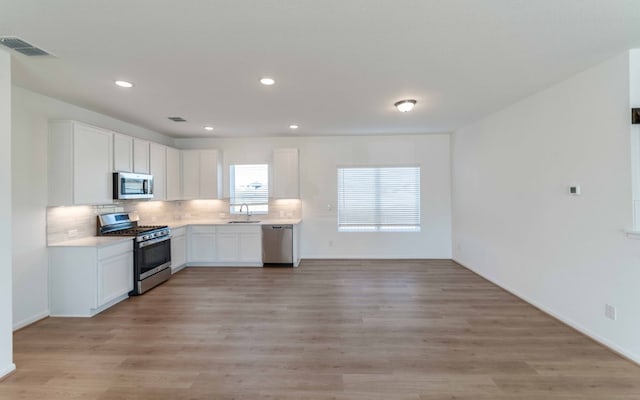 kitchen featuring white cabinets, sink, backsplash, appliances with stainless steel finishes, and light wood-type flooring