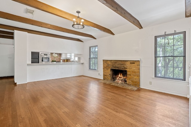 unfurnished living room featuring beamed ceiling, a fireplace, light hardwood / wood-style flooring, and a healthy amount of sunlight