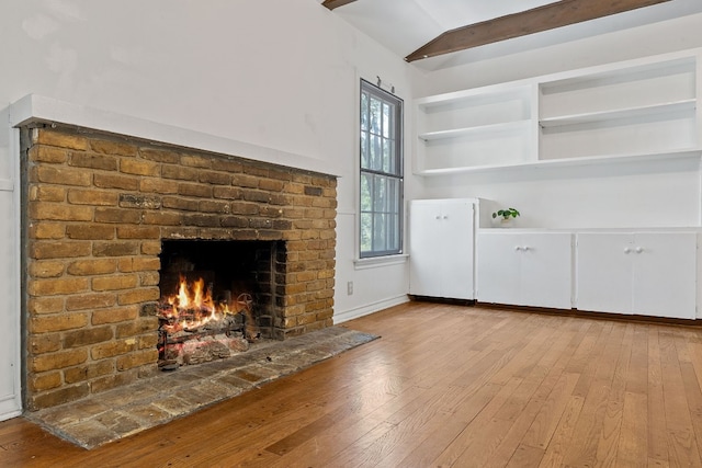 unfurnished living room featuring a brick fireplace, brick wall, lofted ceiling with beams, and light hardwood / wood-style floors