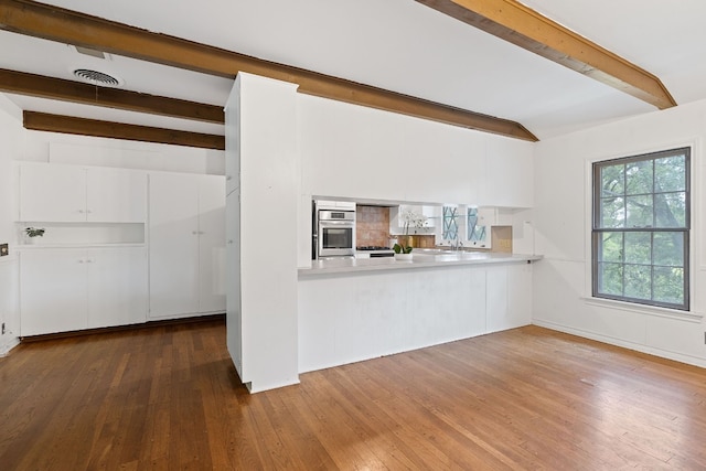 interior space with beam ceiling, kitchen peninsula, hardwood / wood-style flooring, and oven