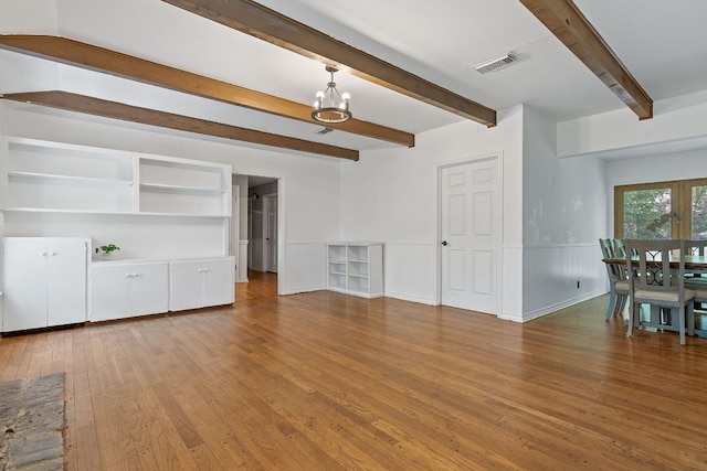 unfurnished living room featuring beam ceiling, hardwood / wood-style flooring, and a chandelier