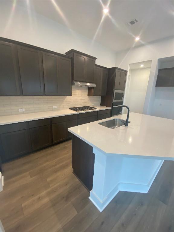 kitchen with sink, stainless steel appliances, tasteful backsplash, a center island with sink, and dark hardwood / wood-style flooring