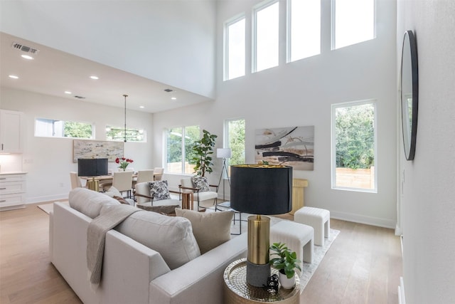 living room featuring light hardwood / wood-style floors, a towering ceiling, and a healthy amount of sunlight