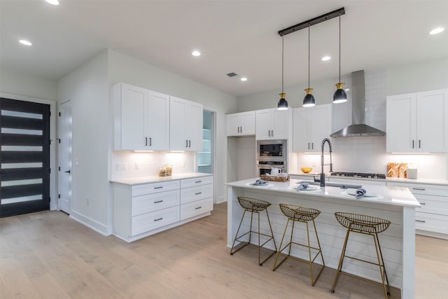 kitchen with backsplash, light hardwood / wood-style flooring, stainless steel appliances, wall chimney range hood, and white cabinets