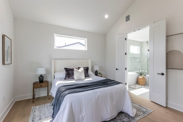 bedroom with light hardwood / wood-style floors, lofted ceiling, and ensuite bath