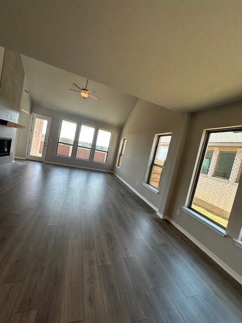 unfurnished living room with dark wood-type flooring, a fireplace, baseboards, and ceiling fan