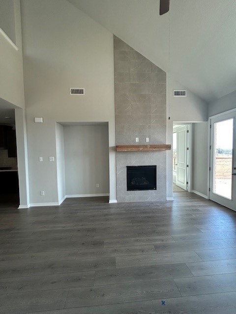 unfurnished living room featuring dark wood-type flooring, baseboards, high vaulted ceiling, and a tiled fireplace