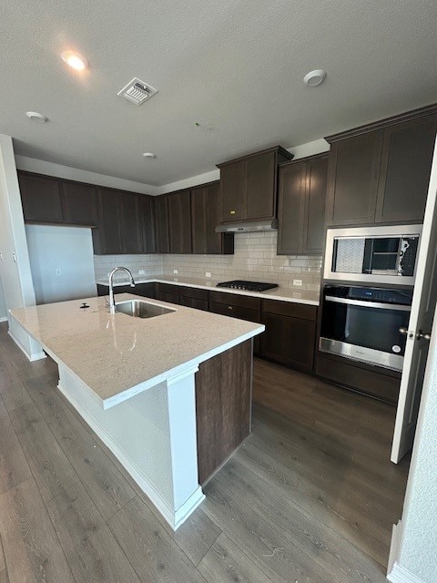 kitchen featuring an island with sink, wood finished floors, stainless steel appliances, under cabinet range hood, and a sink