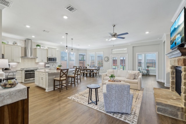 living room with ceiling fan, a stone fireplace, crown molding, light hardwood / wood-style floors, and sink