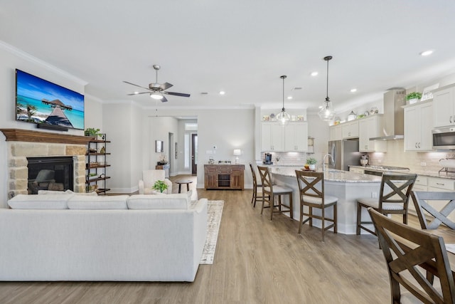 living room featuring light wood-type flooring, a fireplace, ornamental molding, ceiling fan, and sink