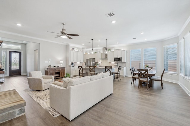 living room featuring ceiling fan, crown molding, light wood-type flooring, and a fireplace