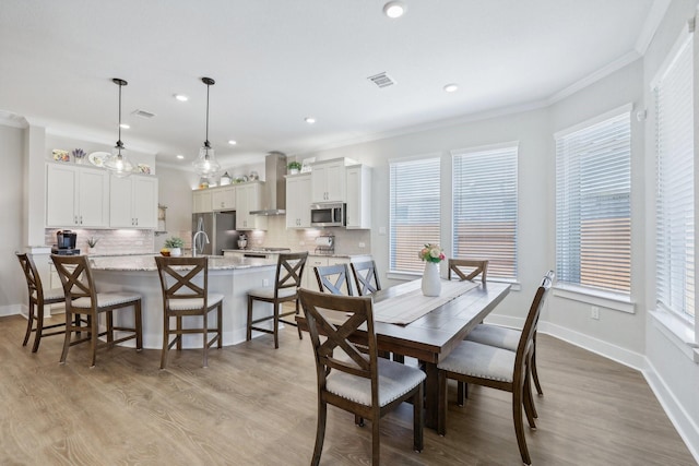 dining space with light wood-type flooring, plenty of natural light, and crown molding