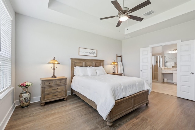 bedroom with ceiling fan, multiple windows, hardwood / wood-style floors, and a tray ceiling