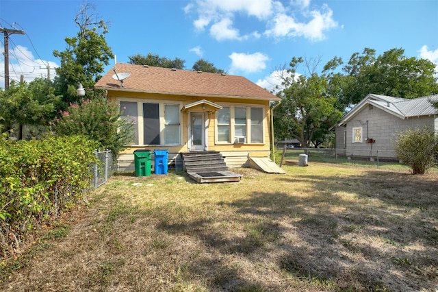 rear view of house featuring entry steps, roof with shingles, a lawn, and a fenced backyard