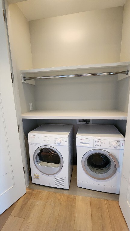 laundry area with washing machine and clothes dryer and light wood-type flooring