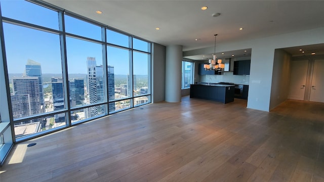 unfurnished living room with dark wood-style floors, a view of city, floor to ceiling windows, a notable chandelier, and recessed lighting