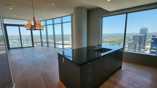 kitchen with dark hardwood / wood-style flooring, hanging light fixtures, a kitchen island with sink, sink, and an inviting chandelier