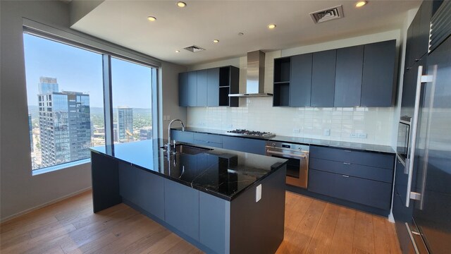 kitchen with light hardwood / wood-style flooring, appliances with stainless steel finishes, wall chimney range hood, and sink