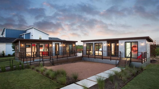 back of house at dusk with a lawn, a patio, a wooden deck, and fence