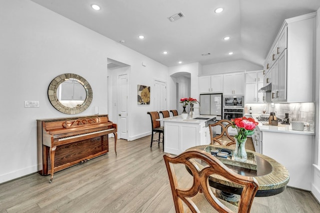 kitchen featuring appliances with stainless steel finishes, a center island with sink, light wood-type flooring, and backsplash