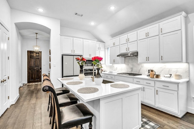 kitchen with hardwood / wood-style floors, vaulted ceiling, stainless steel appliances, and a kitchen island with sink