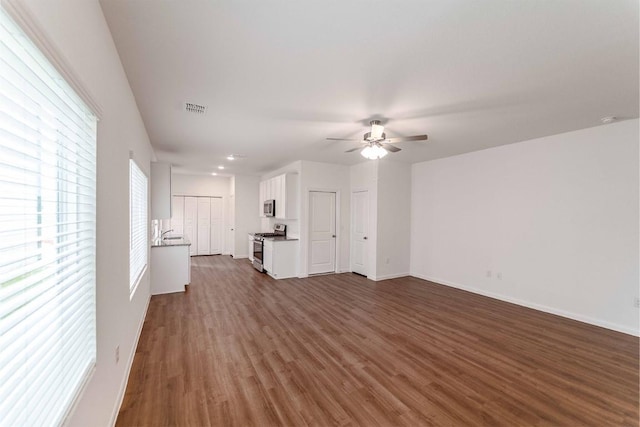 unfurnished living room with dark wood-style floors, baseboards, visible vents, and a ceiling fan