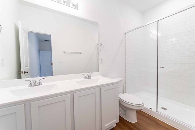 bathroom featuring dual vanity, wood-type flooring, a shower with door, and toilet