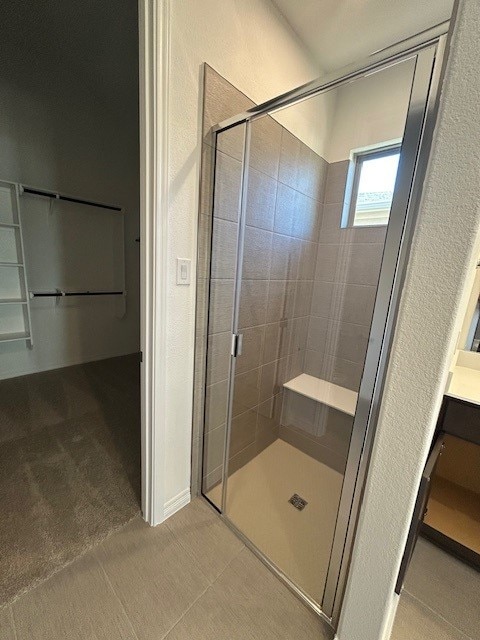 full bath with tile patterned flooring, a shower stall, and a walk in closet