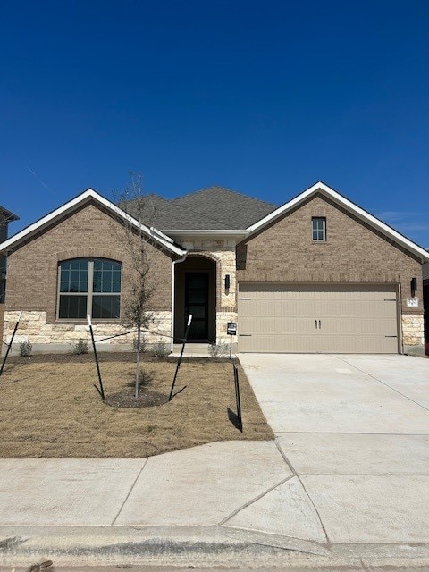 single story home featuring a garage, brick siding, driveway, and a shingled roof