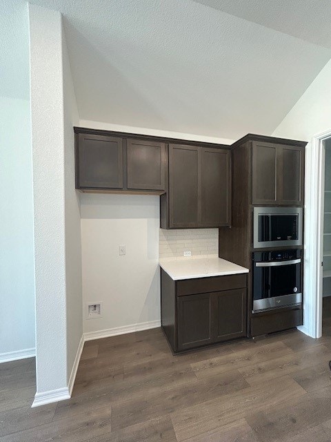 kitchen featuring lofted ceiling, dark brown cabinetry, stainless steel appliances, and dark wood-style flooring