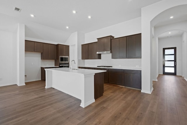 520 Raleigh Dr, Georgetown, TX 78633 - kitchen with arched walkways, a kitchen island with sink, decorative backsplash, stainless steel appliances, and dark brown cabinets