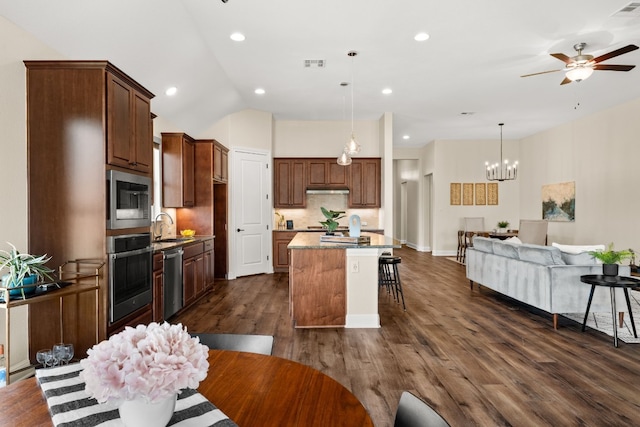 kitchen with appliances with stainless steel finishes, vaulted ceiling, dark wood-type flooring, a center island, and hanging light fixtures