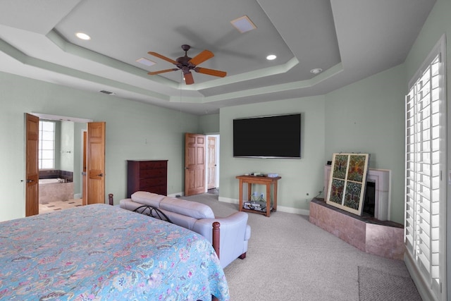 bedroom with light colored carpet, ceiling fan, a tray ceiling, and ensuite bathroom