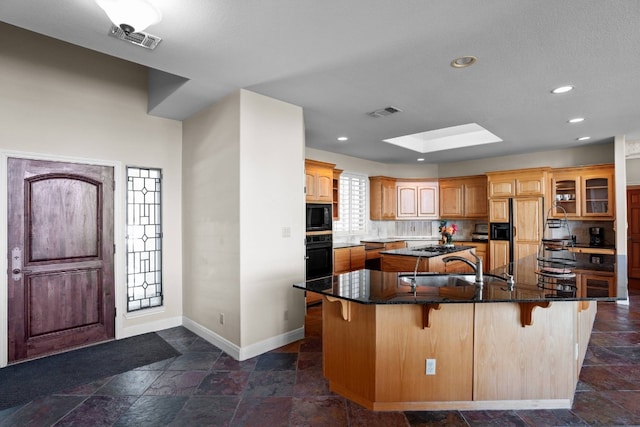 kitchen with a kitchen bar, backsplash, a skylight, black appliances, and a large island with sink